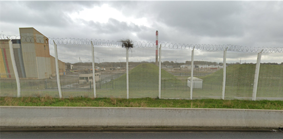 A fence with razor wire and barbed wire on the side of a road. Within the razor wire and barbed wire, there is a nest.