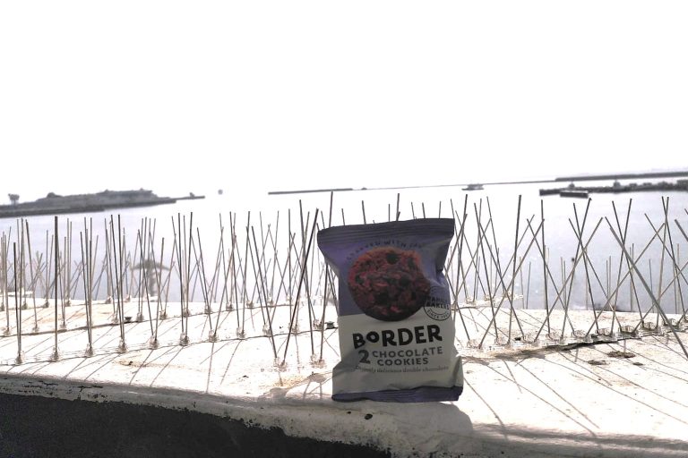 Photo of pack of "Border" biscuits sits on anti-seagull spikes by the window. The port of Dover is visible in the background.