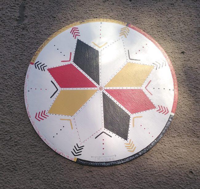 Paint on wood artwork representing an eight point start coloured in white, black, red and yellow.